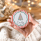 Hand holding a red stripe ceramic tree ornament personalized with Emily 2026