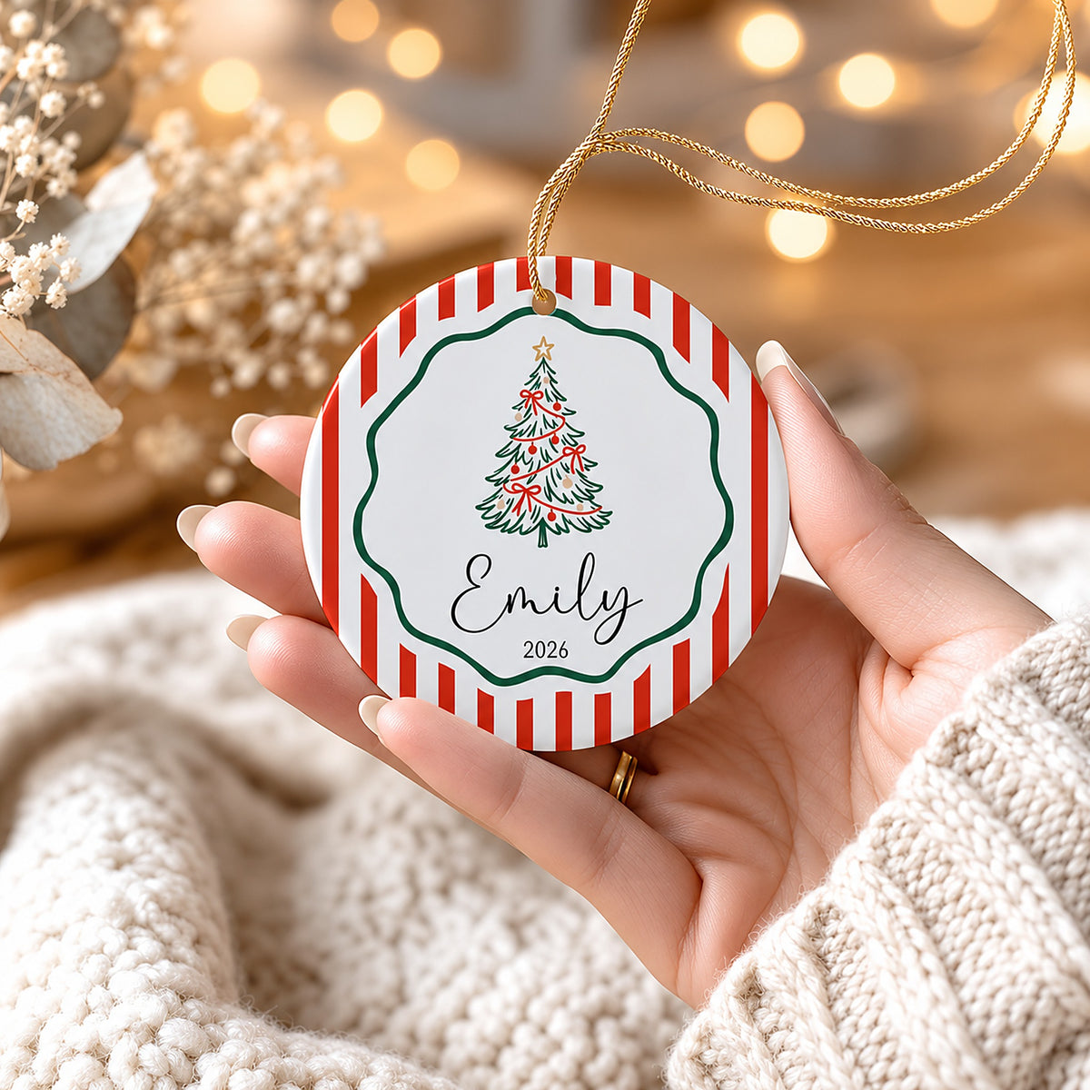 Hand holding a red stripe ceramic tree ornament personalized with Emily 2026